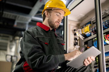 Poster - Young serious engineer in workwear and hardhat scrolling through technical data