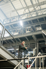 Poster - Bald mature engineer or foreman in workwear standing over staircase in factory