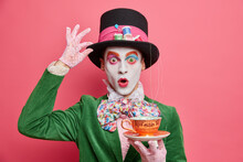 Surprised Male Hatter Wears Gentlemans Clothes Holds Cup Of Hot Tea Pretends To Come From Wonderland Wears Vivid Makeup Celebrates Halloween On Costume Party Poses Indoor Alone. Body Painting