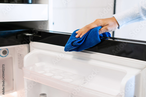 Woman hand with micro fiber cloth wiping refrigerator surface. Home, housekeeping concept.