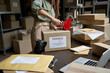 © insta_photos - Female post mail storage worker holding tape dispenser sealing shipping online store order courier delivery cardboard box packing ecommerce fragile dropshipping parcel in distribution warehouse.