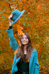 Wall Mural - Close-up portrait of a beautiful girl in a gray coat and gray hat, standing next to colorful autumn leaves. A work of art by a romantic woman.