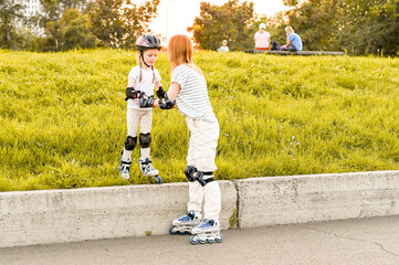 Young mother and her daughter rollerskating in summer day