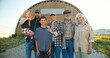 © VAKSMANV - Portrait happy Caucasian family of three generations standing outdoor at farm shed and smiling to camera. Old parents with children and grandchildren in countryside. Farmers. Summer. Village lifestyle