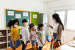 © JR-50 - A group of Kids students wearing masks lined up waiting for woman teachers to Check Fever by Digital Thermometer in the classroom for Scan and Protect from Coronavirus Outbreak - Healthcare Concept