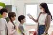 © JR-50 - A group of Kids students wearing masks lined up waiting for woman teachers to Check Fever by Digital Thermometer in the classroom for Scan and Protect from Coronavirus Outbreak - Healthcare Concept