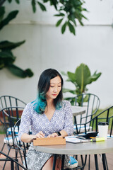 Wall Mural - Pretty young Chinese businesswoman sitting at cafe table, drinking coffee and working with reports and documents