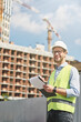 © Kostiantyn - Good job. Young happy civil engineer or construction supervisor wearing helmet looking away and smiling while inspecting building site and making some notes