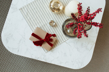 Wall Mural - Handmade paper gift box with red ribbon bow-tie, red berries in glass vase on marble table. Flat lay, top view.