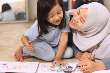 Asian muslim mother drawing with her daughter, single mom teaching baby girl, learning on the floor, happy family