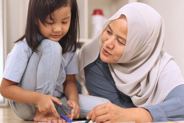 Asian muslim mother drawing with her daughter, single mom teaching baby girl, learning on the floor, happy family