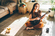 Woman playing music with ukulele at home, relaxation and recreation concept.