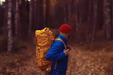 Wall Mural - man with  backpack a view from the back, hiking in the forest, autumn landscape, the back of  tourist with a backpack