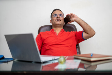 technology, remote job and lifestyle concept - happy indian man in glasses with laptop computer working at office.