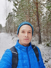 selfie portrait of a russian man in a blue jacket and hat in winter in the forest