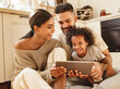 © JenkoAtaman - happy multi ethnic family: parents and son laughed and watch funny video on a tablet  at home.