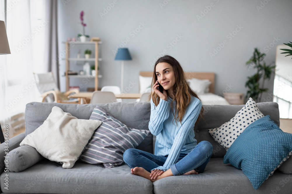 Smiling woman talking to mobile on the sofa. Online conversation. - obrazy, fototapety, plakaty 
