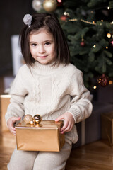 Wall Mural - Smiling child girl 4-5 year old sitting under Christmas tree with decorations in room close up. New Year. Winter holiday season.