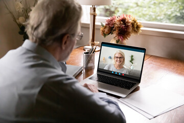 Wall Mural - Rear view of elderly man speak talk on video call on laptop with smiling mature woman. Old husband have webcam digital conference with Caucasian middle-aged wife on computer. Virtual event concept.