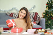 © chinnarach - close up young asian woman showing wrapped gift box sitting in living room with pine tree decoration for merry Christmas and happy new year festival season concept