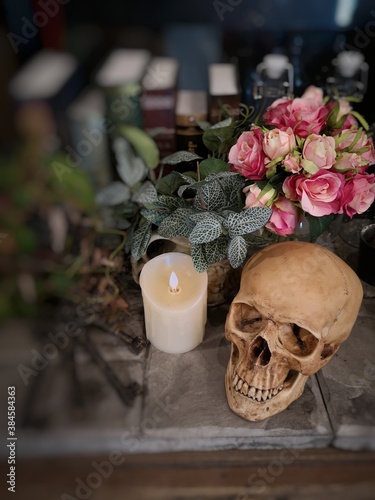 Halloween still life : The human skull with white candle light, vintage key chain, bottle, books, roses bouquet in vase and ornamental plants on wood