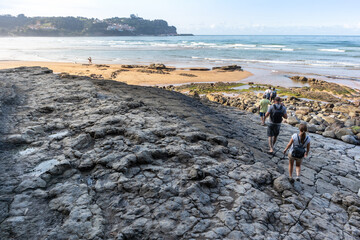 Ancient dinosaur footprints on dry mud by the beach. Old archeological site from the Jurassic period, sauropod prints. People visiting the site on summer. Playa de la Griega, Asturias, North of Spain