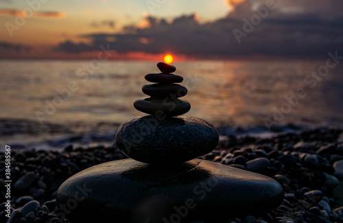 pyramid or tower of pebble stones with the sun on top against the background of the sea and the sunset sky. Zen stones, balance and meditation concept, background
