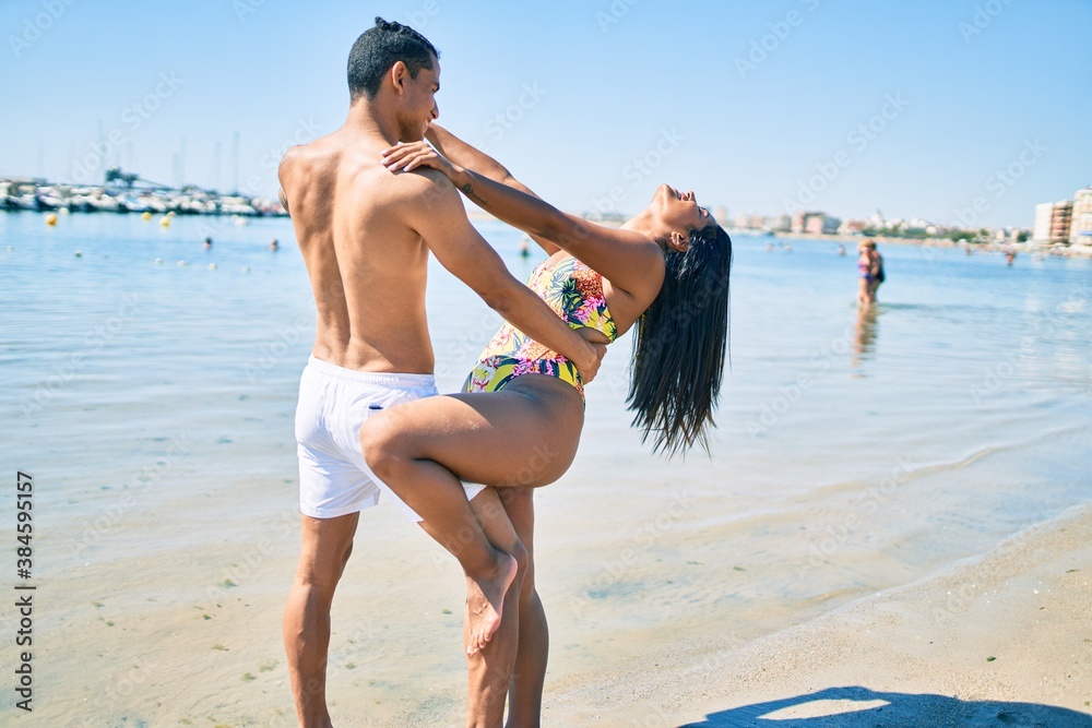 Young latin couple wearing swimwear  smiling happy and dancing at the beach.