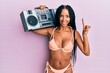 Beautiful hispanic woman wearing bikini holding boombox smiling with an idea or question pointing finger with happy face, number one
