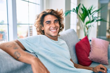 Wall Mural - Young hispanic man smiling happy sitting on the sofa at home