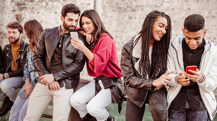 Wall Mural - group of different young people having fun talking, joking and bonding together watching contents on smartphones screens.  Multiracial millennial generation students using technologies concept.