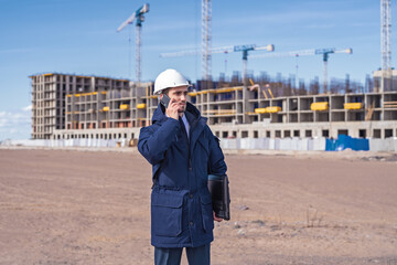 Wall Mural - a civil engineer in a white helmet is talking on the phone in the background of construction.