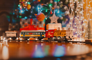 toy vintage steam locomotive on the floor under a decorated Christmas tree on a background of bokeh lights garland.