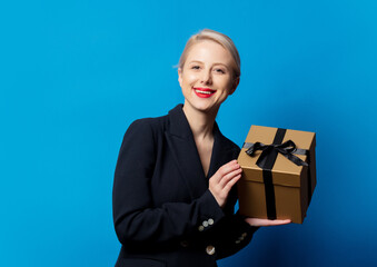 Wall Mural - Style blonde in black jacket with gift box on blue background