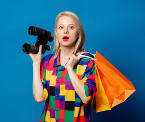 Wall Mural - Blonde girl in 90s shirt  with binoculars and shopping bags