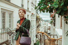 Outdoor Autumn Portrait Of Young  Fashionable Woman Wearing Trendy Brown Leather Beret, Turtleneck, Green Velour Blazer, Holding Textured Purple Bag, Posing In Street Of Paris. Copy Space 