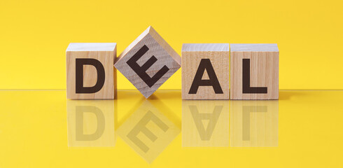 Sticker - Word Deal is made of wooden building blocks lying on the table and on a light yellow background.