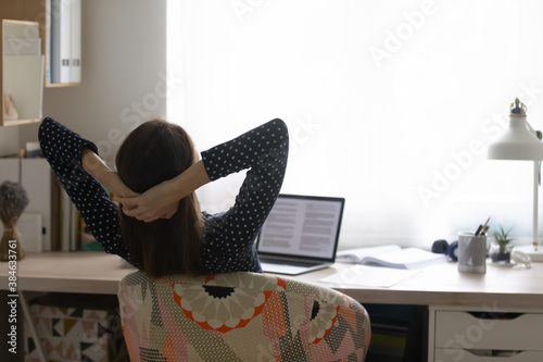 Rear back view young woman folded hands behind head, relaxing on comfortable chair at home office. Distracted from distant study or remote job millennial girl daydreaming, enjoying stress free time.