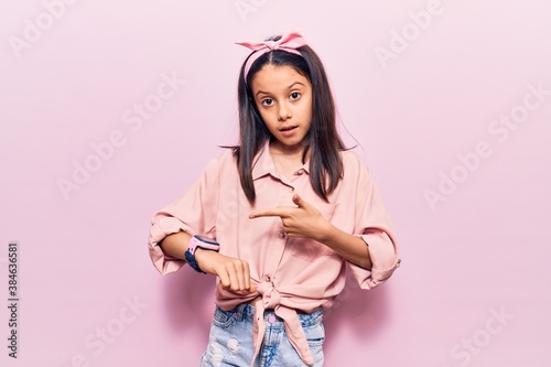 Fototapeta Beautiful child girl wearing casual clothes in hurry pointing to watch time, impatience, upset and angry for deadline delay