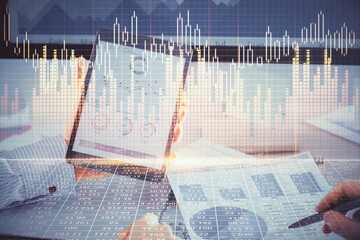 Double exposure of man's hands holding and using a digital device and forex graph drawing. Financial market concept.