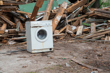 View Of The Dump Of Parts Of An Old Wooden House. In The Foreground Is A Broken And Dirty White Washing Machine. Background.