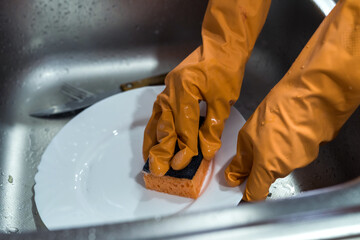 Female hand in gloves washing dishes over the sink in the kitchen