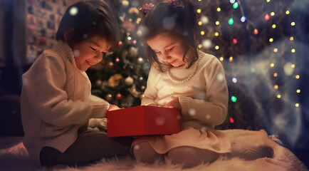 Family on Christmas eve at fireplace. Kids opening Xmas presents. Children under Christmas tree with gift boxes. Decorated living room with traditional fire place. Cozy warm winter evening at home.