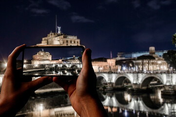 Wall Mural - Tourist taking photo of Castle of Holy Angel in Rome, Italy. View of Castle of Angel illuminated with the ancient bridge at night.