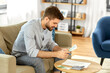 business, finances, accounting and people concept - man with money and calculator filling papers at home