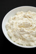© Liudmyla - Tasty Ricotta Cheese in a white bowl on a black background, low angle view. Close-up.