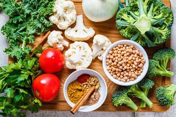 Canvas Print - Cooking background of fresh vegetables, spices and beans. Raw ingredients for cooking vegetarian curry with vegetables and chickpeas on a wooden board, top view.