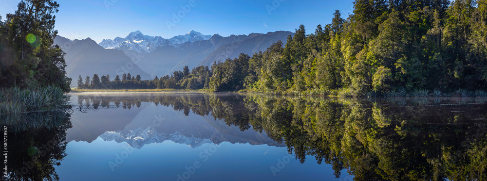 Fox glacier. Mountains. Lake Matheson mirror lake; New Zealand. Oceania. Morninglight. Panorama. Snow covered mountains. Forest. Reflections. - obrazy, fototapety, plakaty 