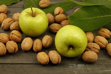 Green ripe apples and walnuts lie on a wooden table under green walnut leaves