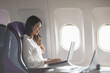 © 220 Selfmade studio - Asian young woman using laptop sitting near windows at first class on airplane during flight,Traveling and Business concept